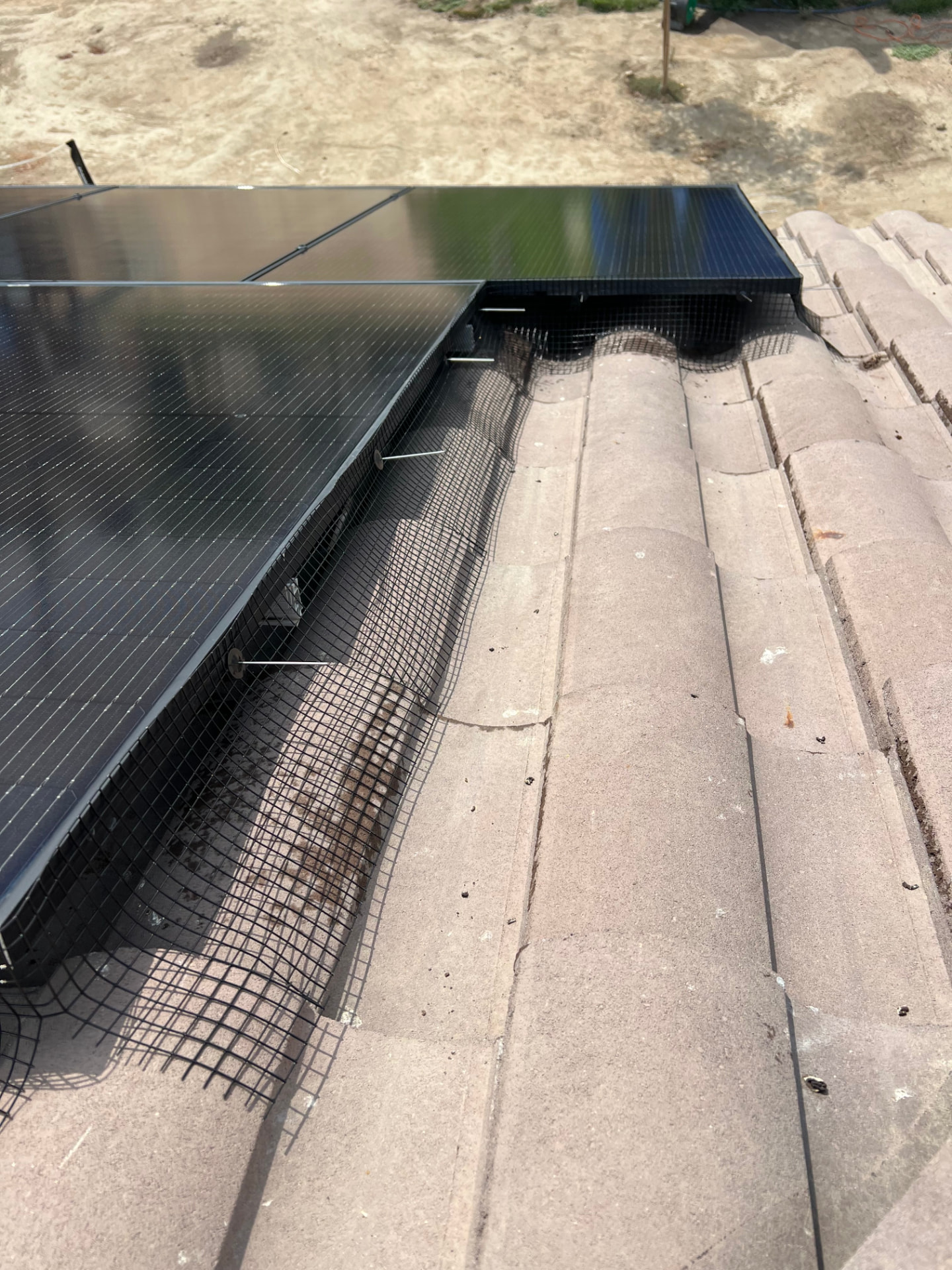 Bird guard mesh secured under solar panels on a tile roof