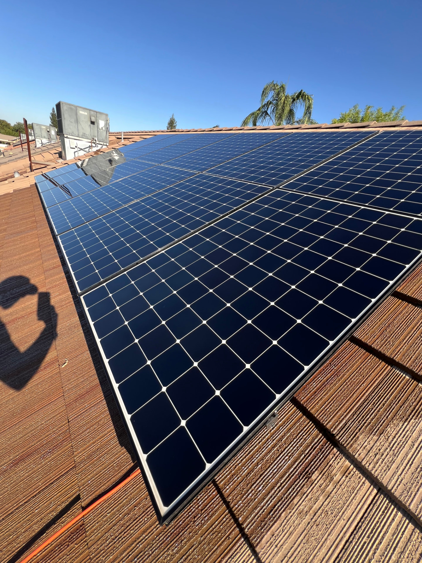 Close-up of spotless dark solar panels on a red tile roof under a clear blue sky