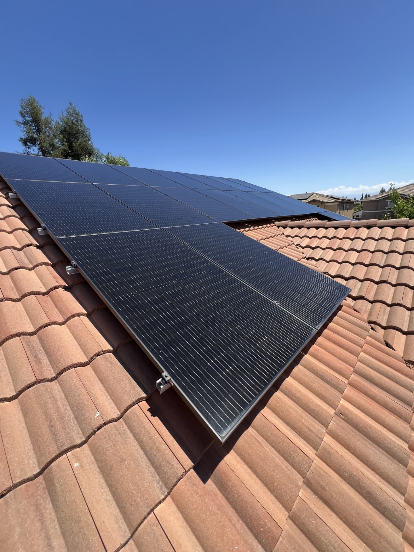 Long row of black solar panels washed clean on a red tile roof