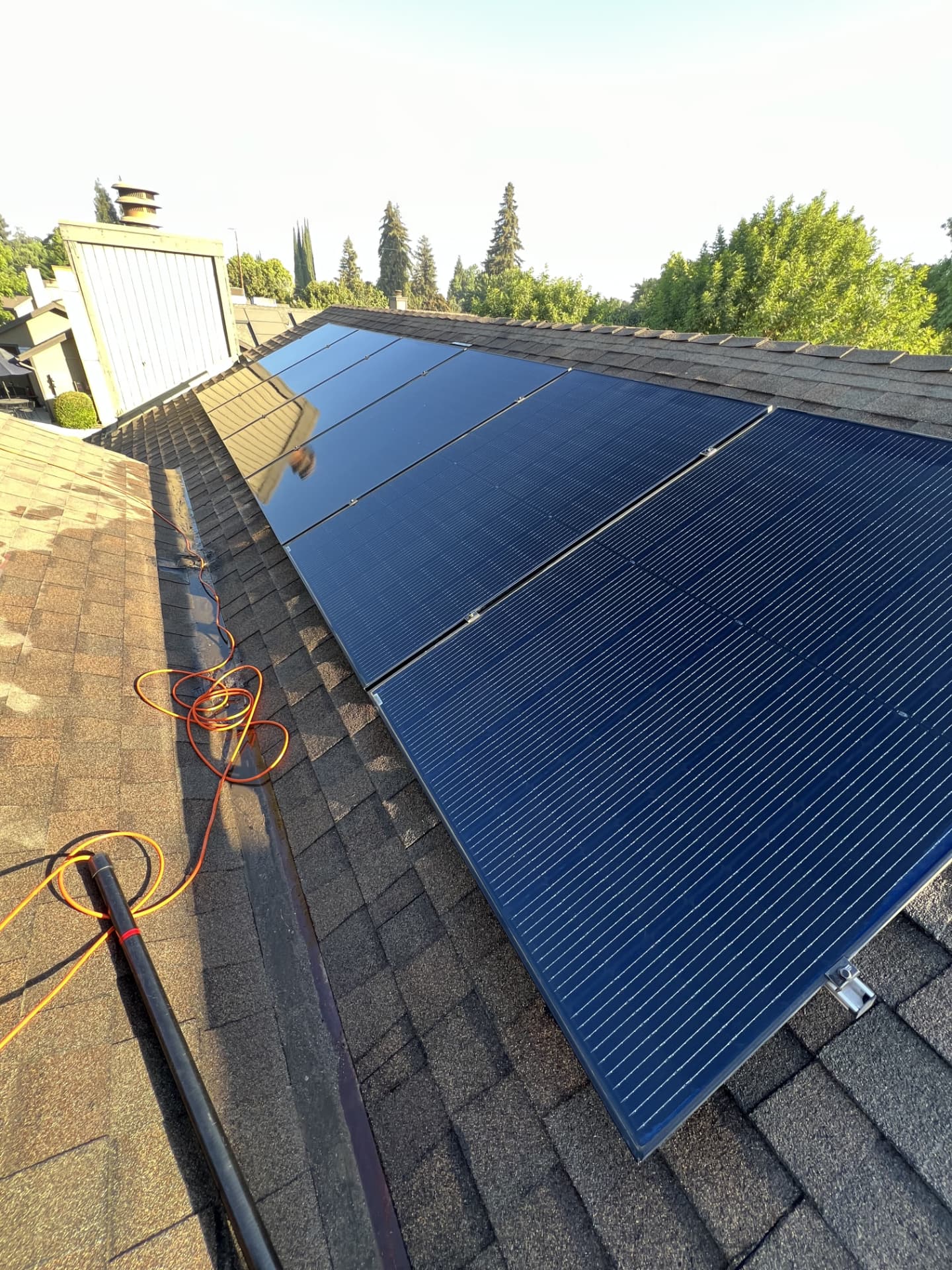 All-black solar panels freshly washed on a shingle roof at golden hour