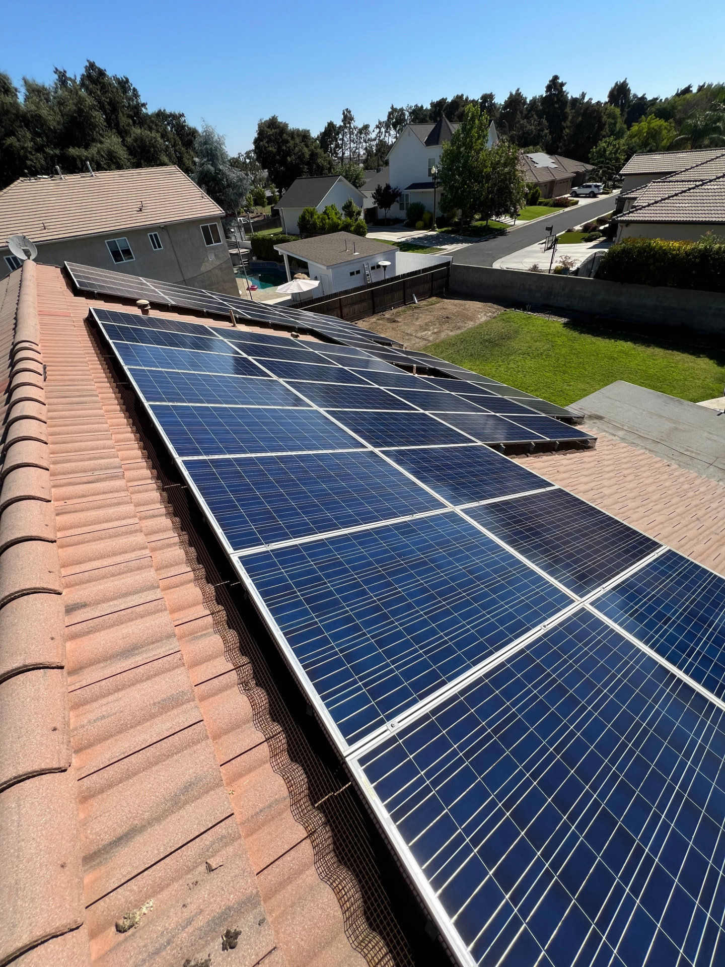 Large solar array with bird guard mesh along the lower edge on a red tile roof overlooking a neighborhood